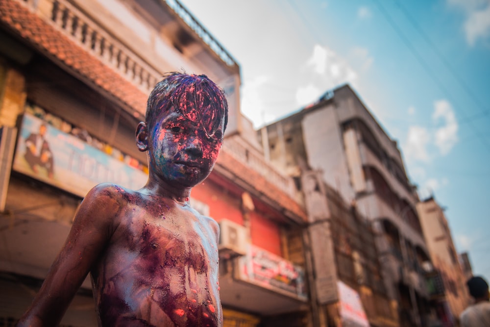 man with blue face paint in front of brown concrete building during daytime
