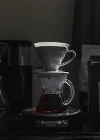A sleek pour-over setup with a glass carafe and kettle on a kitchen counter bathed in morning light.