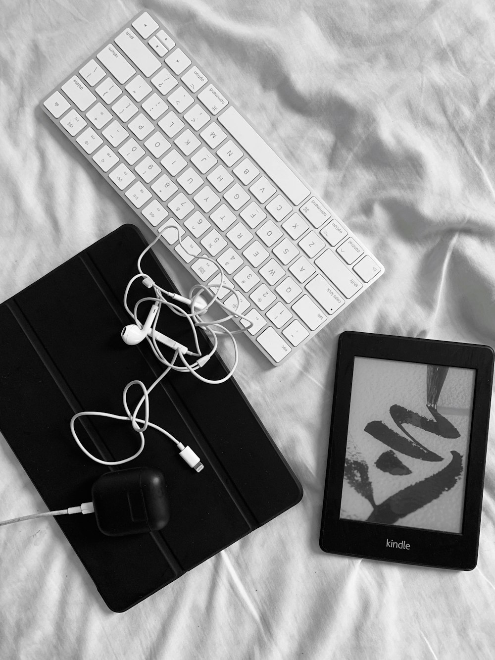 black ipad beside apple keyboard and apple earpods on white textile