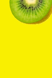 A close-up image of a kiwi slice with vibrant green flesh and small black seeds against a bright yellow background.