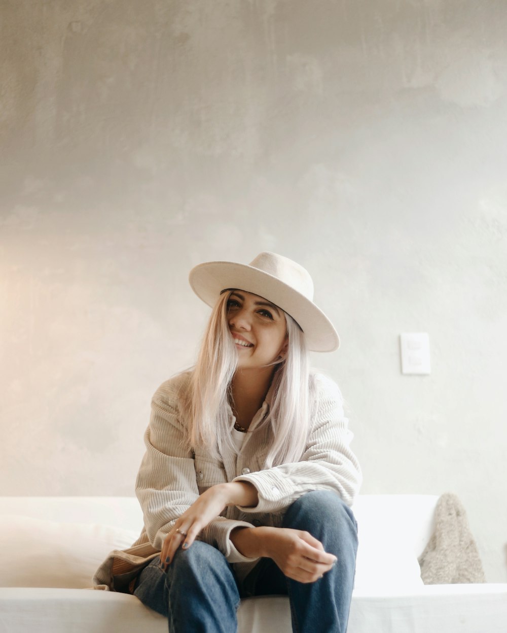 woman in white long sleeve shirt and blue denim jeans wearing white hat sitting on white