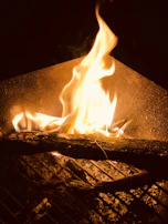 A golden flame flickering over a bed of glowing charcoal, capturing the essence of live fire cooking.