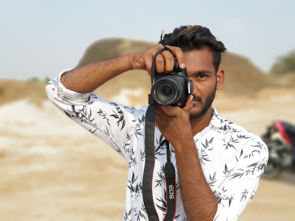 man in white and black floral shirt holding black dslr camera