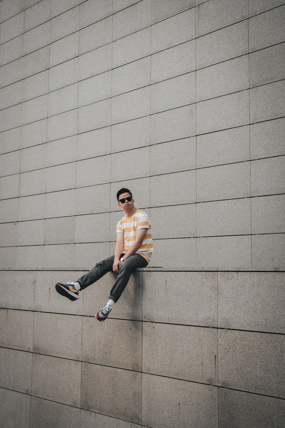 a man sitting on a wall wearing sunglasses