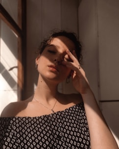 Close-up of relaxed woman with hands gently resting on forehead, golden sunlight filtering softly