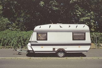 white and brown rv trailer parked on gray asphalt road during daytime