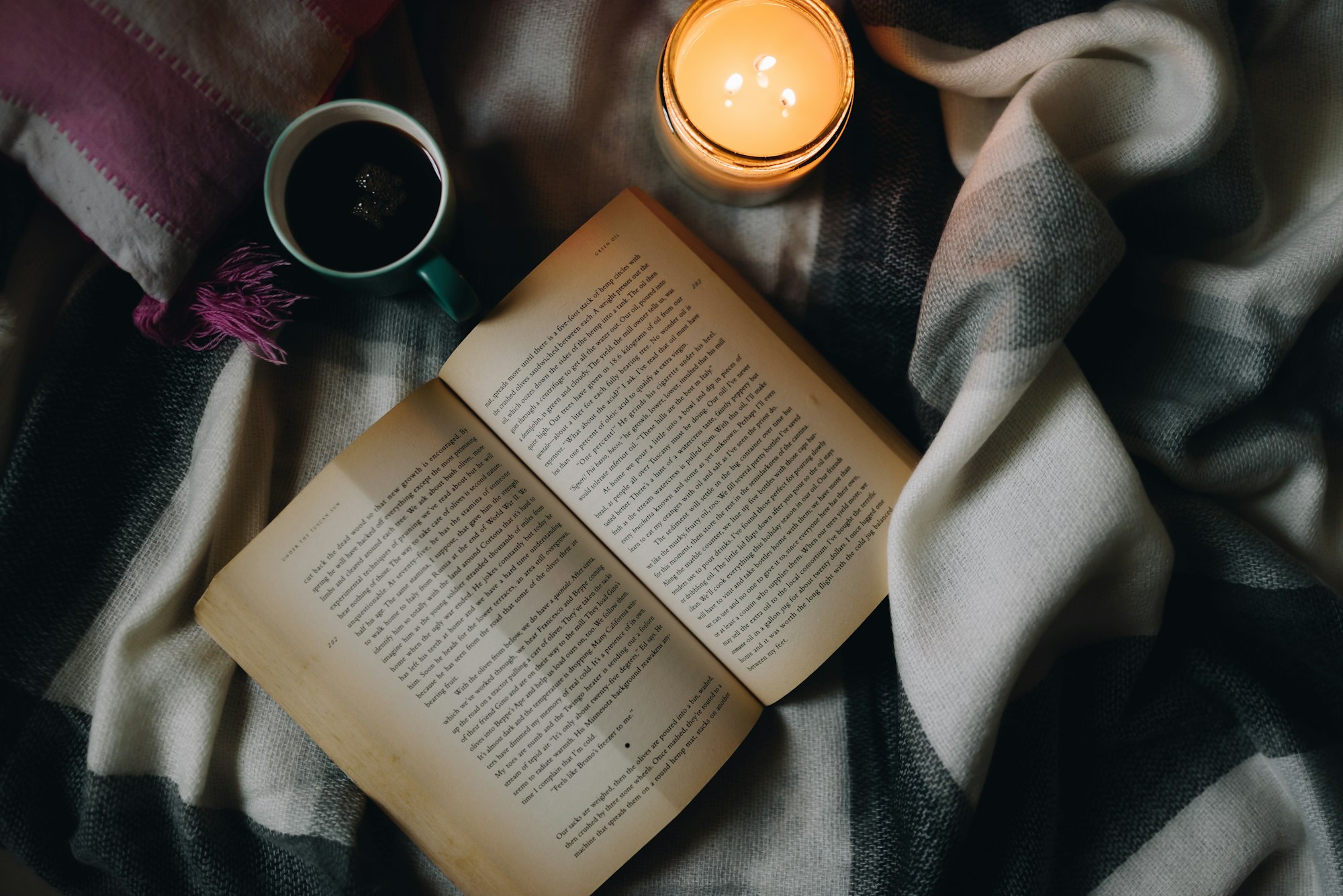 Cozy reading retreat setup with a black ceramic mug of coffee beside an open book on a wooden table