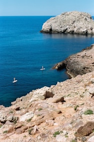 person in white shirt standing on brown rock formation near body of water during daytime