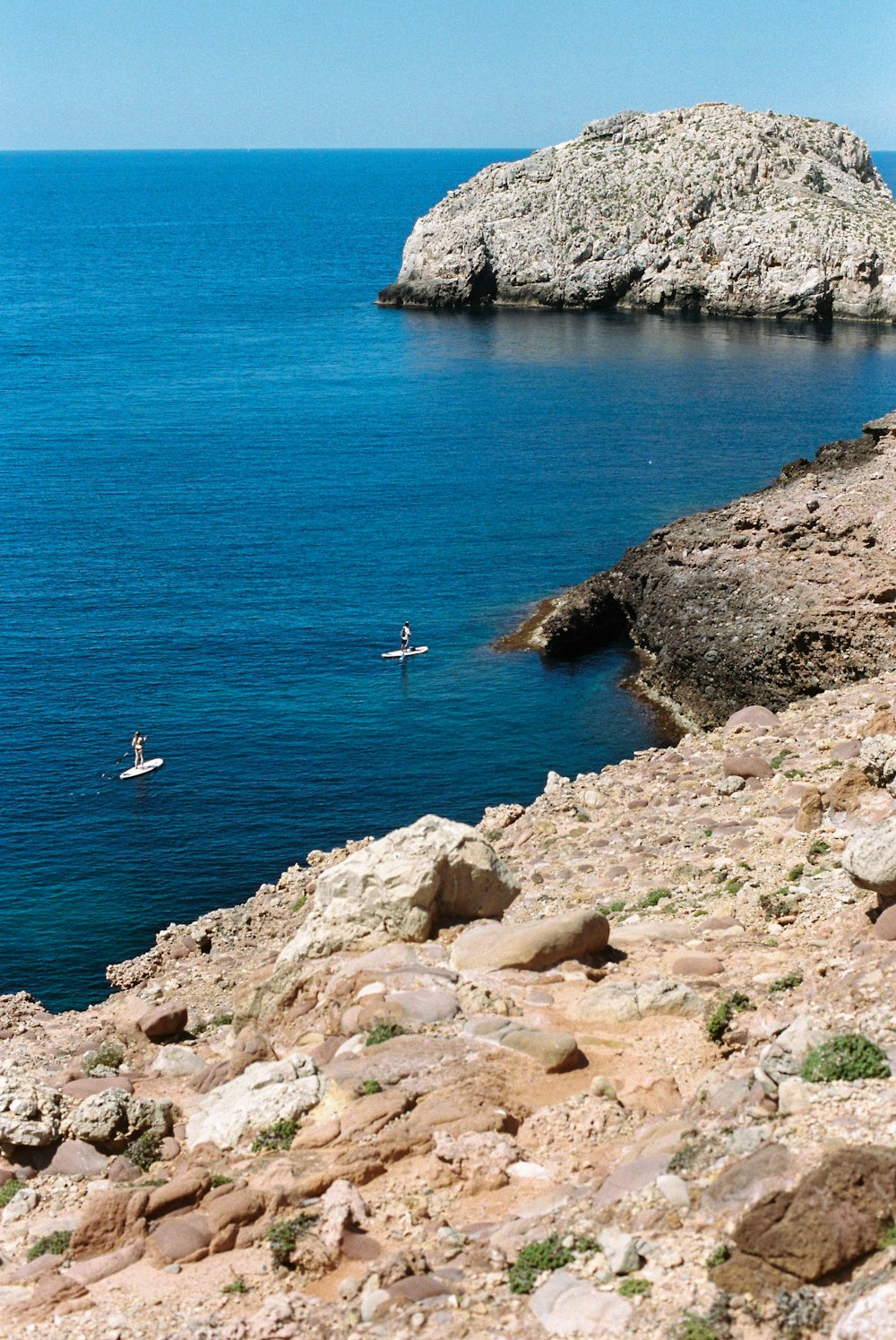 person in white shirt standing on brown rock formation near body of water during daytime