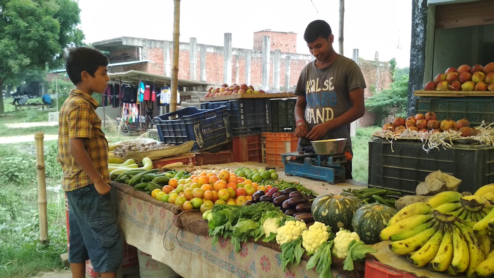 man in red crew neck t-shirt standing in front of fruit stand