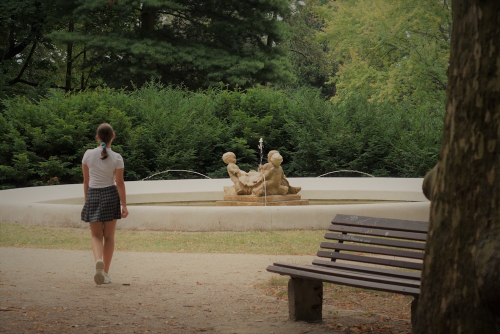 woman in white shirt and black and white striped skirt standing beside brown wooden bench during