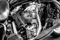A detailed close-up of a motorcycle engine showcasing its chrome components and mechanical intricacies. The image highlights the bike's polished metal parts with clear reflections, along with visible branding and pedal features. The black and white tone emphasizes the contrast between the different elements.