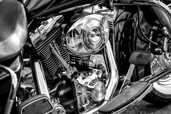 A detailed close-up of a motorcycle engine showcasing its chrome components and mechanical intricacies. The image highlights the bike's polished metal parts with clear reflections, along with visible branding and pedal features. The black and white tone emphasizes the contrast between the different elements.