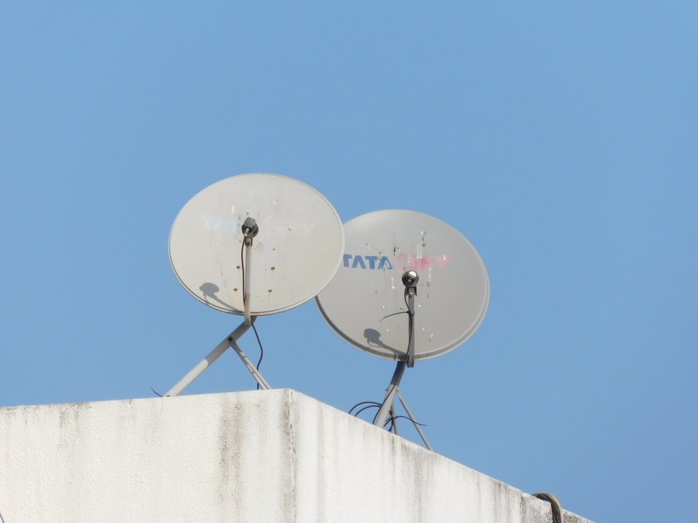 Dos antenas parabólicas grises sobre pared blanca