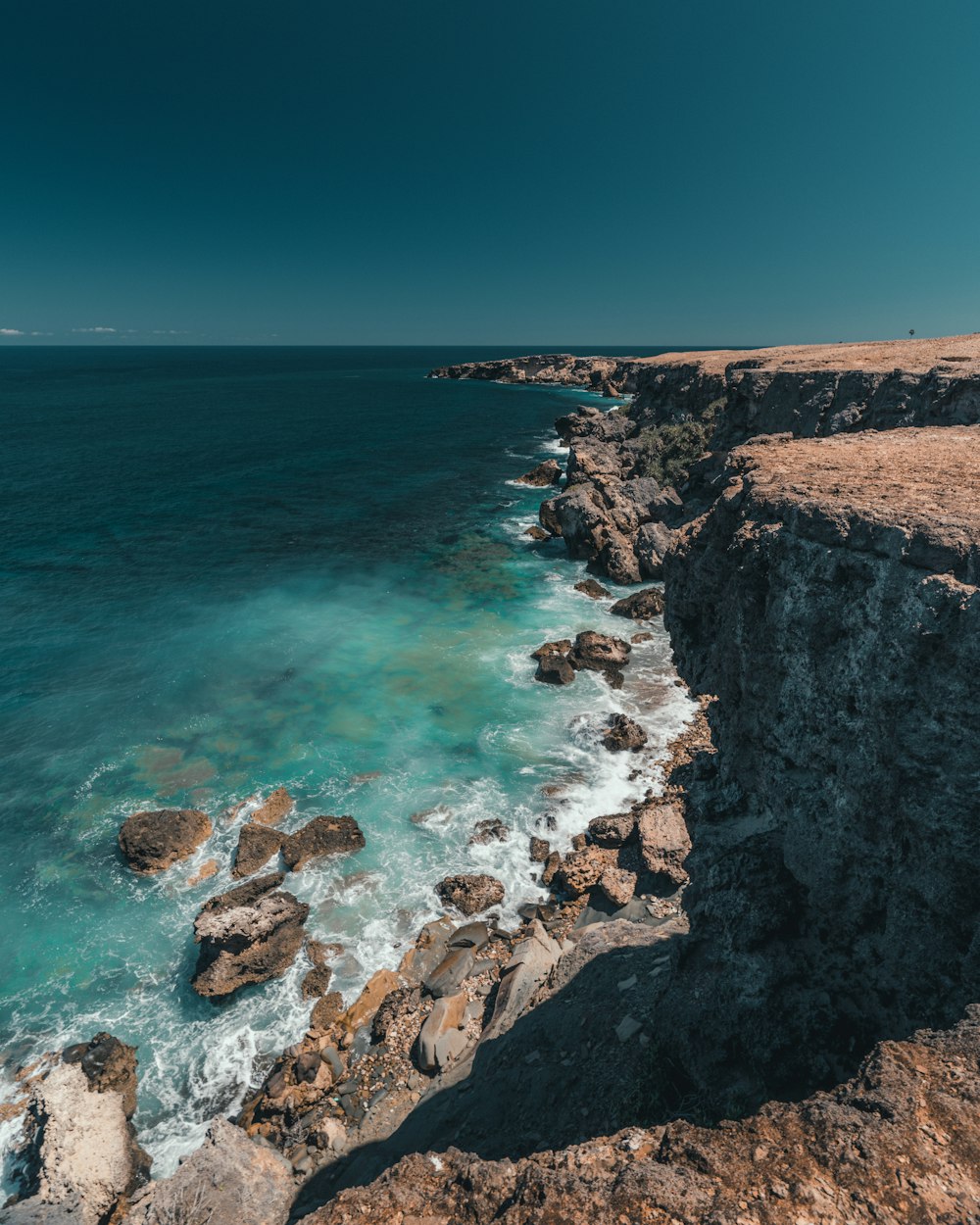 brown rocky mountain beside blue sea under blue sky during daytime