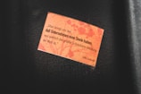 A small rectangular orange paper with a printed quote is attached to a dark surface. The quote is in German and is attributed to Gilles Deleuze. The background of the paper features a subtle pattern resembling floral or organic shapes.