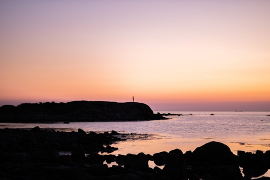silhouette of person standing on rock formation near body of water during sunset in Varberg Sweden