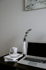 A minimalist workspace featuring a laptop, a notebook, and a cup of coffee beside an open book.