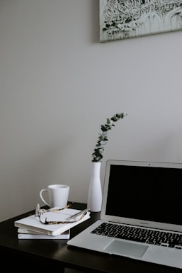A minimalist workspace with a cool, symmetrical vase adding a pop of color next to a laptop and notebook.