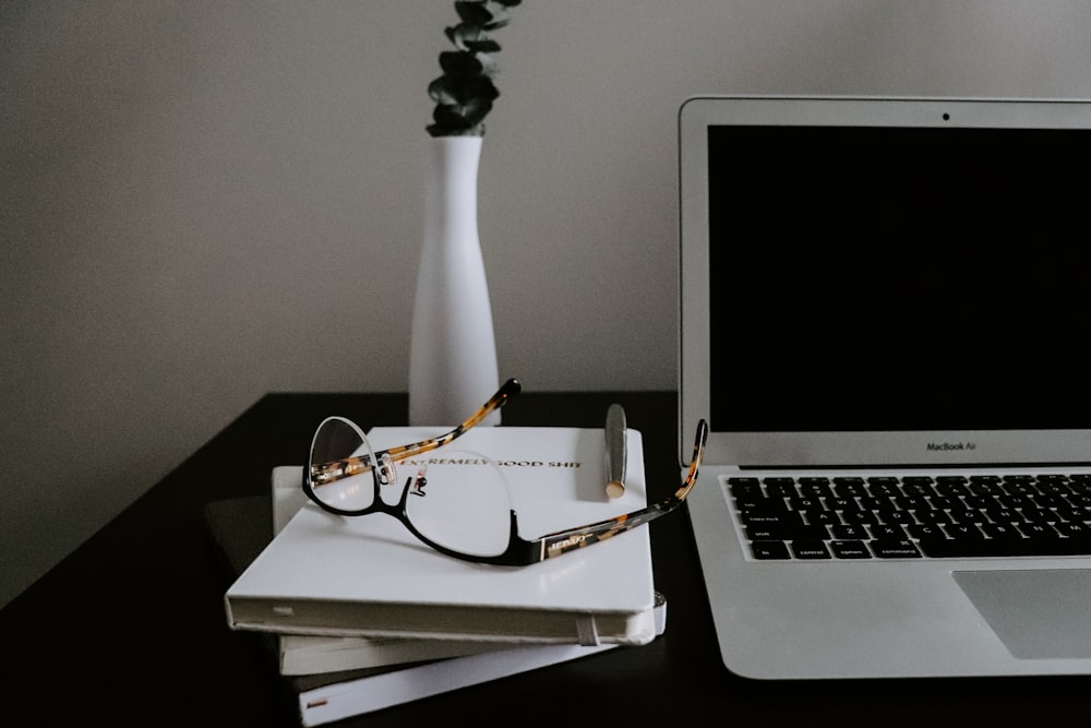 silver macbook air beside eyeglasses on black table