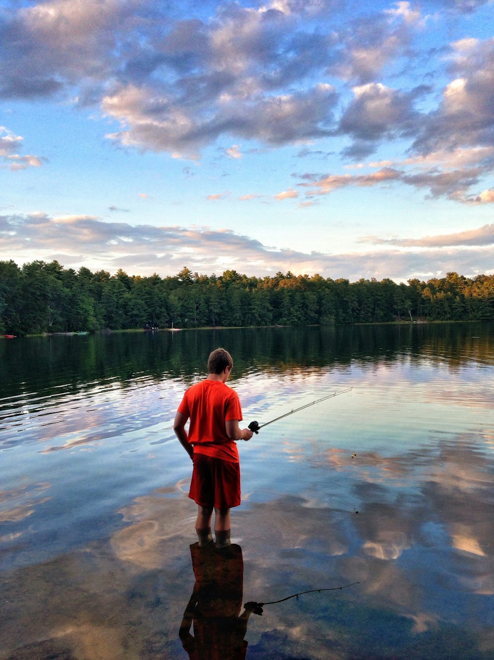 man in red shirt fishing on lake during daytime