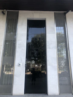 Matte black steel security door with gold accents installed at a modern villa entrance under soft evening light