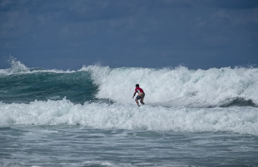 man in red shirt and black shorts surfing on sea waves during daytime