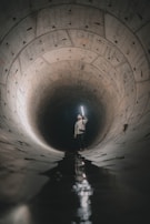 Team members inspecting a large drainage system tunnel with flashlights and safety gear.