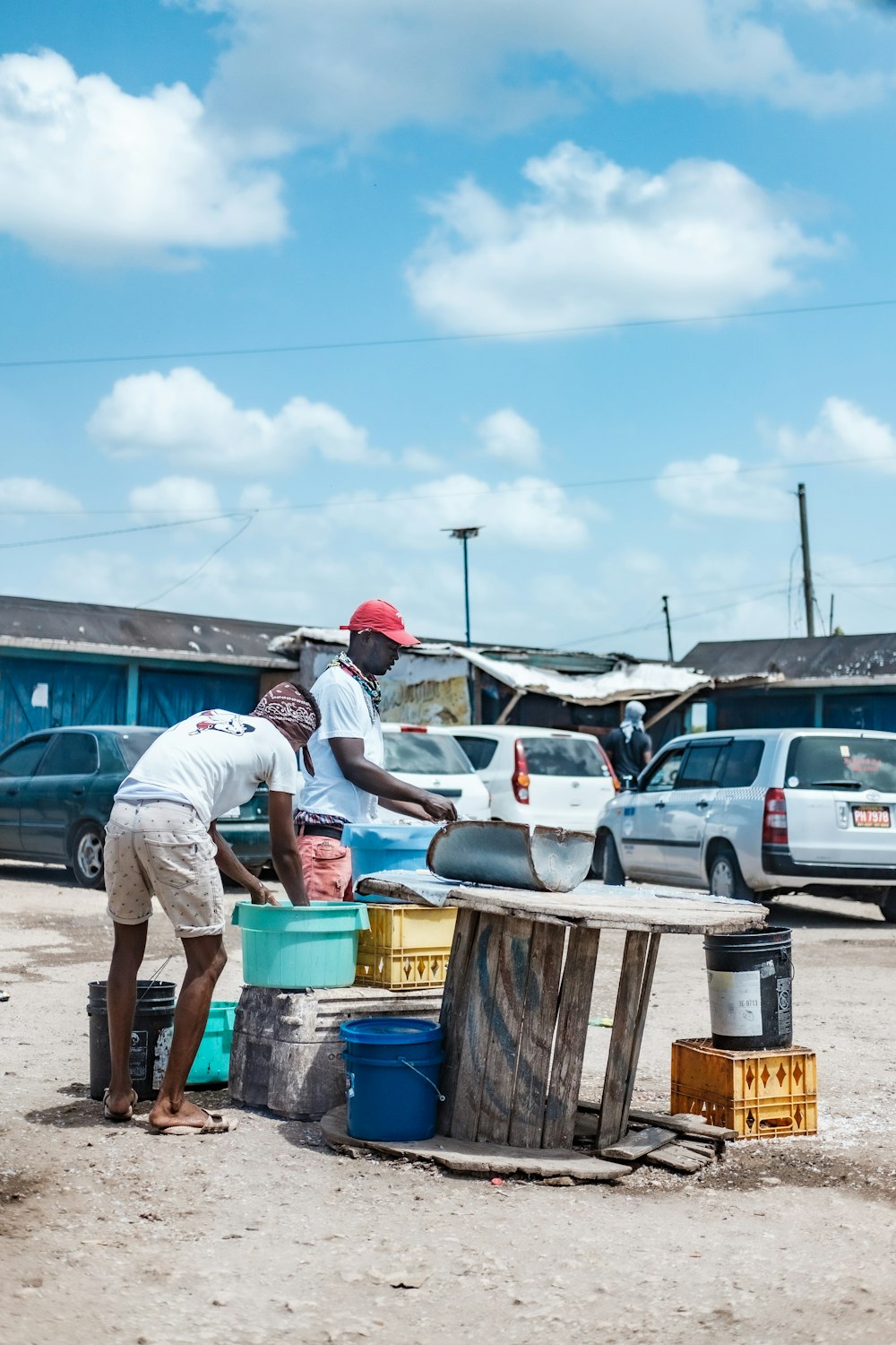 man in white t-shirt and gray pants standing near blue plastic container during daytime