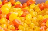 Assorted small, glossy candies with a shiny exterior in vibrant shades of yellow and orange are heaped together, creating a visually appealing, colorful assortment.