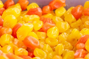 Assorted small, glossy candies with a shiny exterior in vibrant shades of yellow and orange are heaped together, creating a visually appealing, colorful assortment.