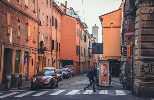 cars parked on sidewalk near buildings during daytime in Bologna Italy