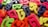 A collection of colorful, plastic Bengali alphabet letters scattered randomly across a brown surface. The letters feature vibrant shades of pink, green, blue, yellow, and orange, creating a lively and playful arrangement.