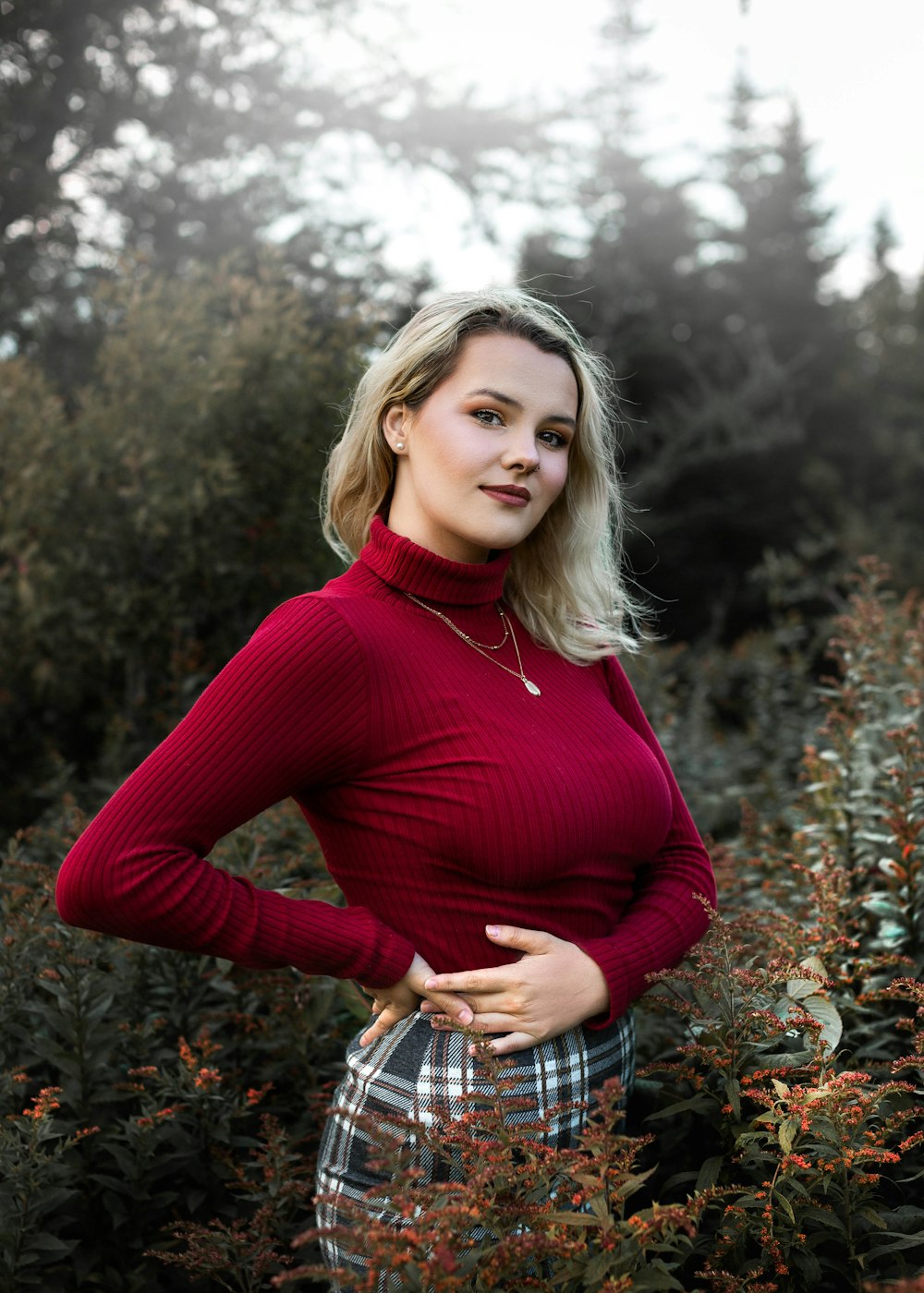 Femme en chemise rouge à manches longues debout sur des feuilles séchées brunes pendant la journée