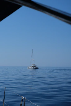 A sleek sailboat cutting through calm blue waters under a clear sky at sunrise.