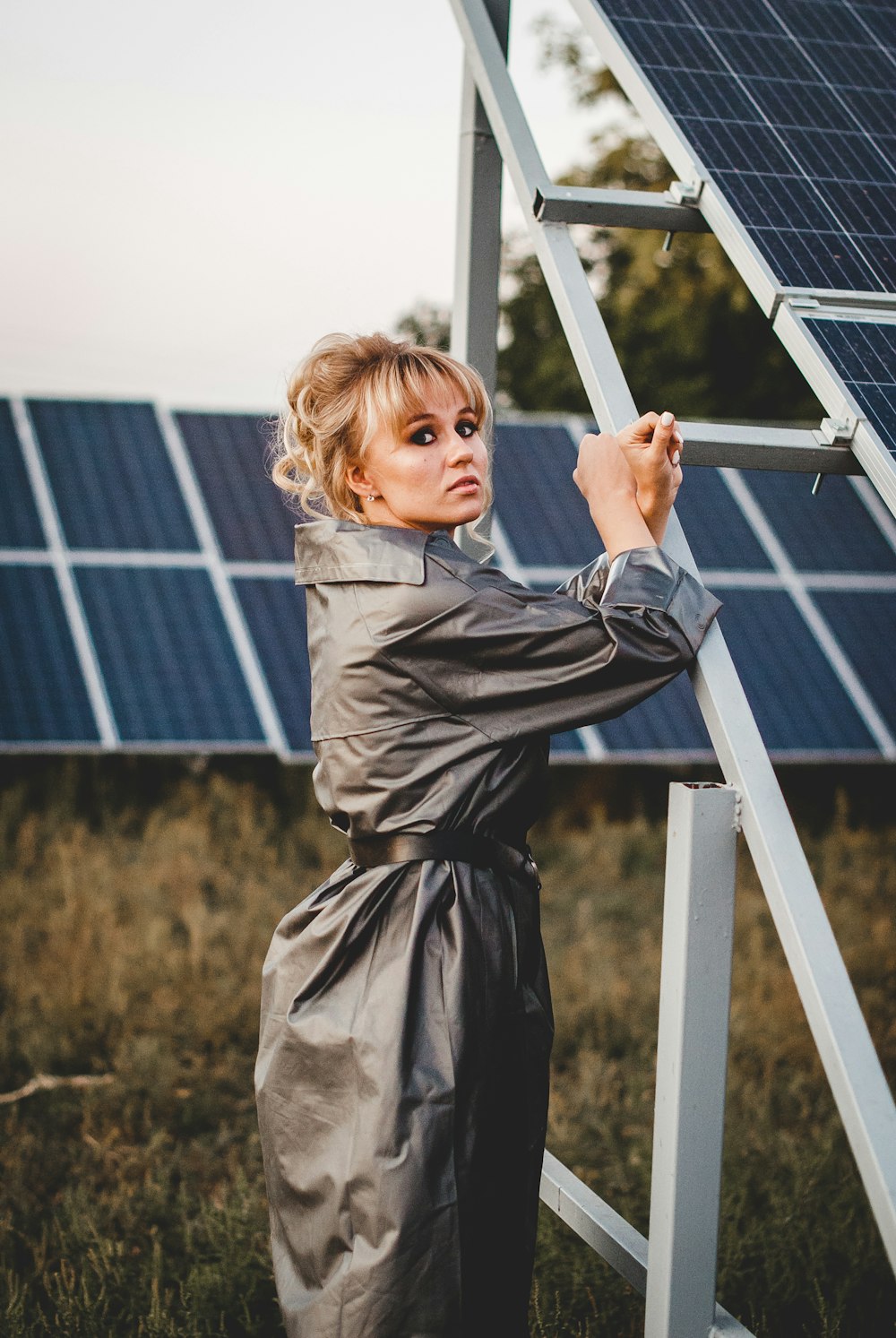 Muchacha con abrigo gris de pie cerca de paneles solares durante el día