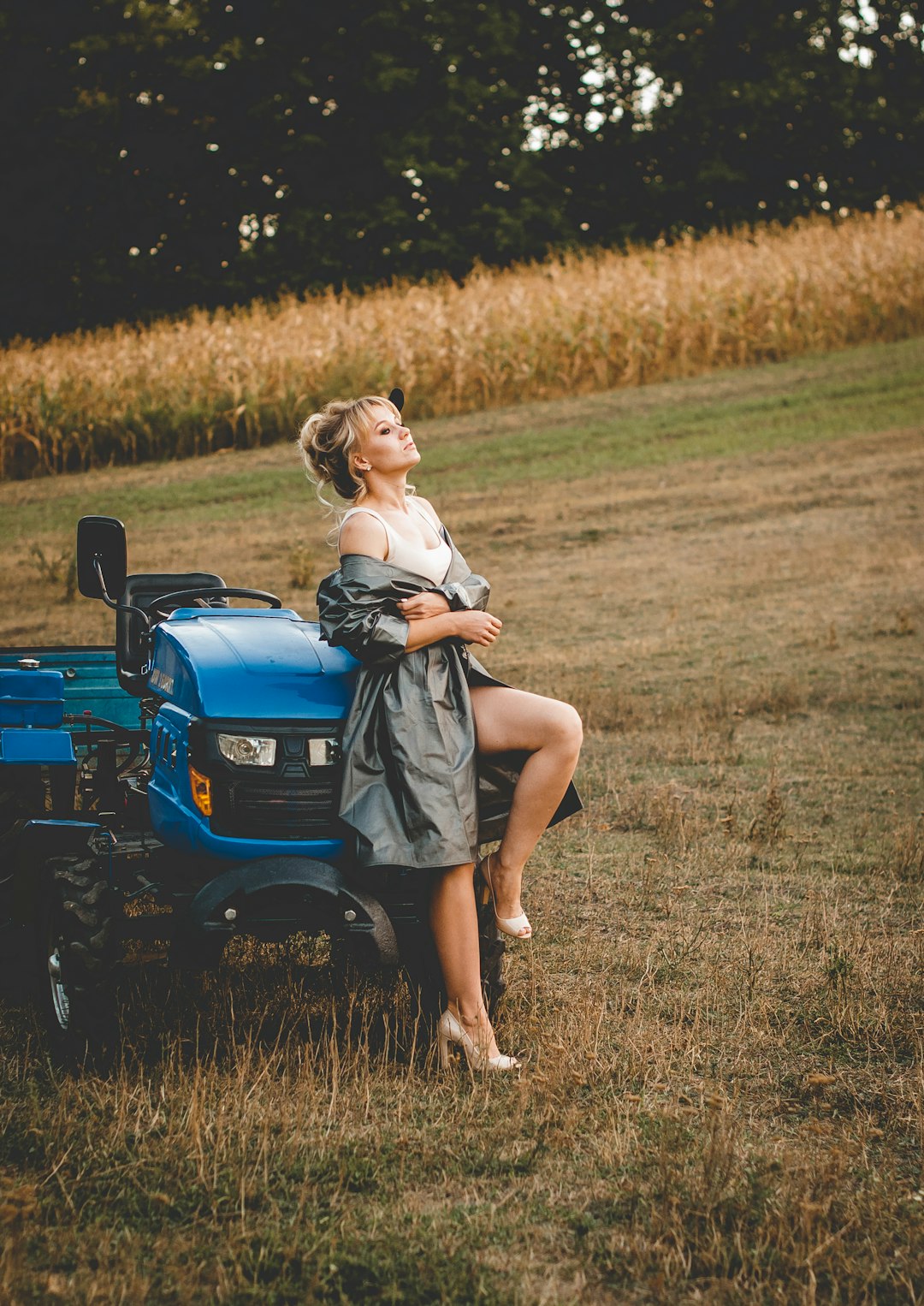 woman in white shirt and gray skirt riding on green tractor on brown grass field during