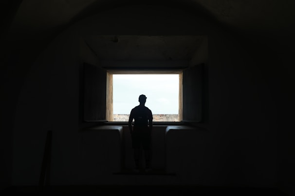 A silhouette of a lone figure watching a storm through a cracked window, the tension palpable.