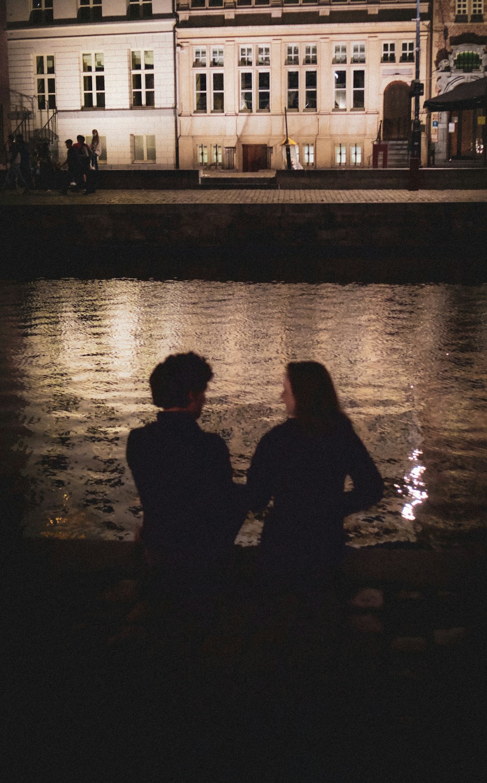 silhouette di uomo e donna in piedi accanto allo specchio d'acqua durante la notte