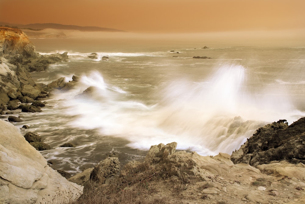 ocean waves crashing on brown rocky shore during daytime