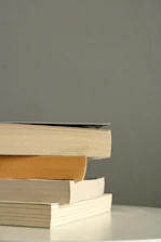 A stack of books and a microphone on a soft pink background.