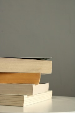 A neatly arranged stack of hardcover academic books with muted earth-tone covers on a wooden desk.
