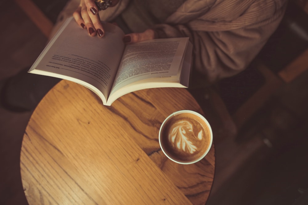 Una persona sentada en una mesa con un libro y una taza de café