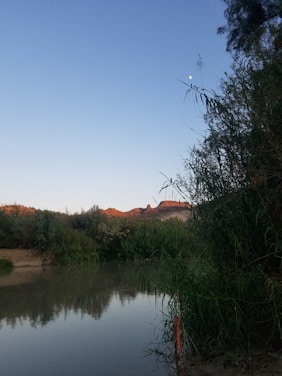 A peaceful West Virginia river winding under a glowing sunset with a bright moon rising over the hills.
