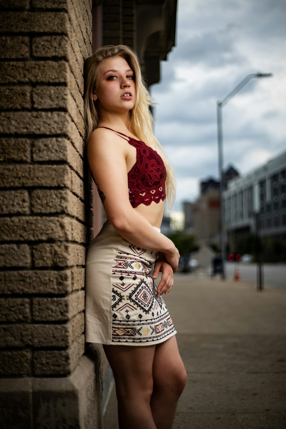 woman in red and white floral halter top dress standing beside brick wall during daytime