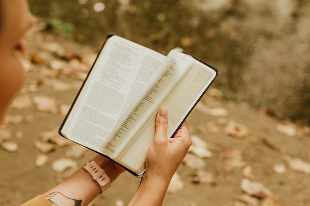 person reading book on brown dirt during daytime