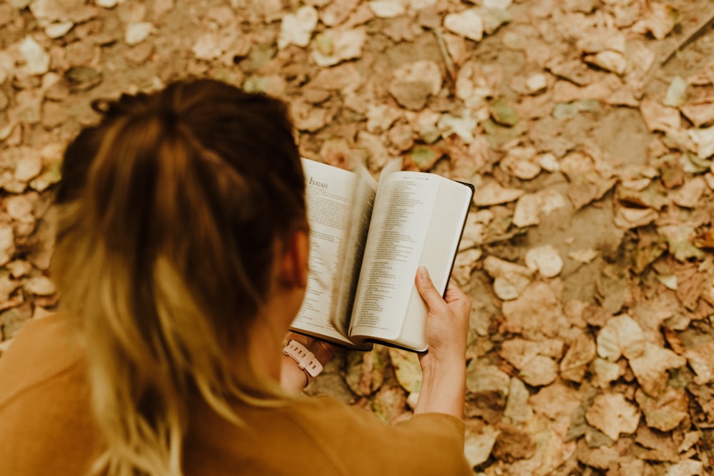 woman reading book on brown leaves