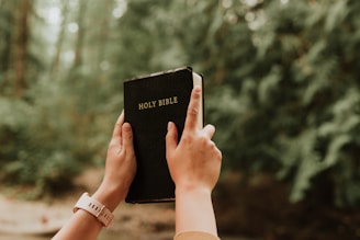 Hands holding a printed copy of a Christian book draft with a peaceful background