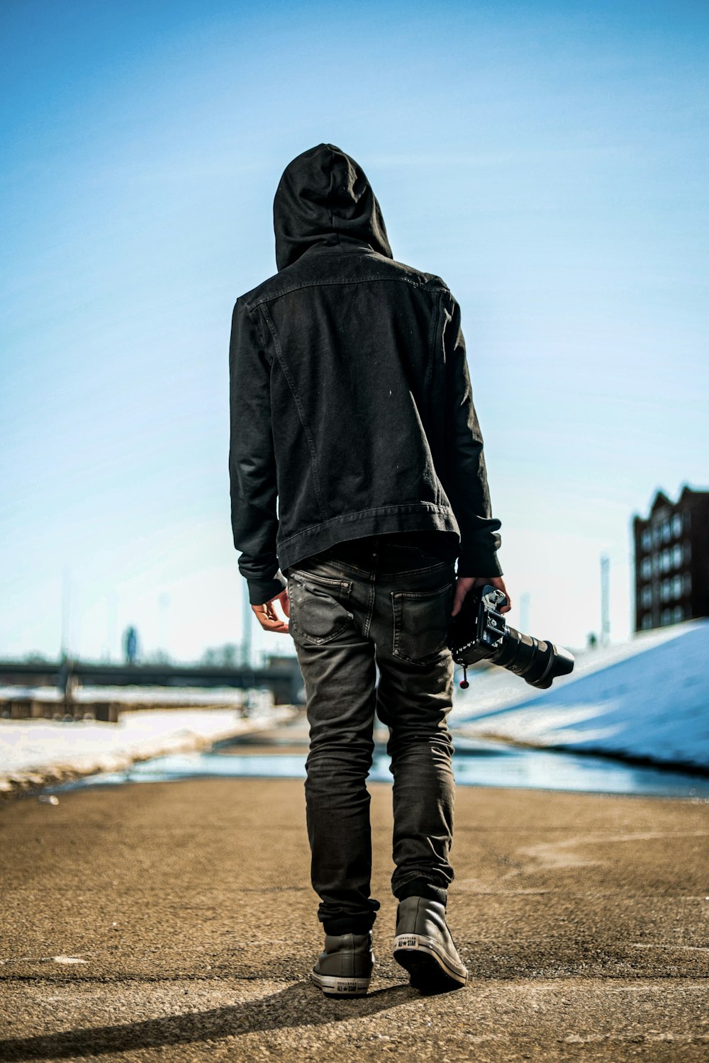 Mann in schwarzem Hoodie und blauer Jeans tagsüber auf braunem Sand