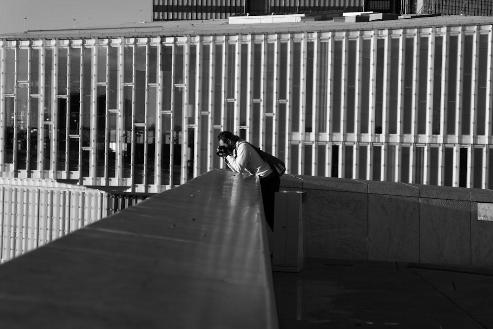 grayscale photo of man in black jacket sitting on concrete bench